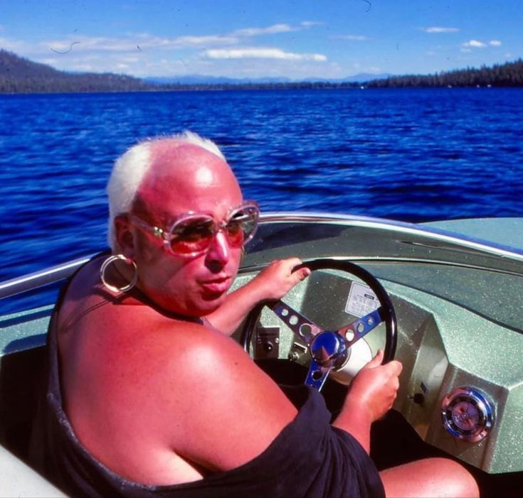 A sunburnt man in pink sunglasses driving a speedboat