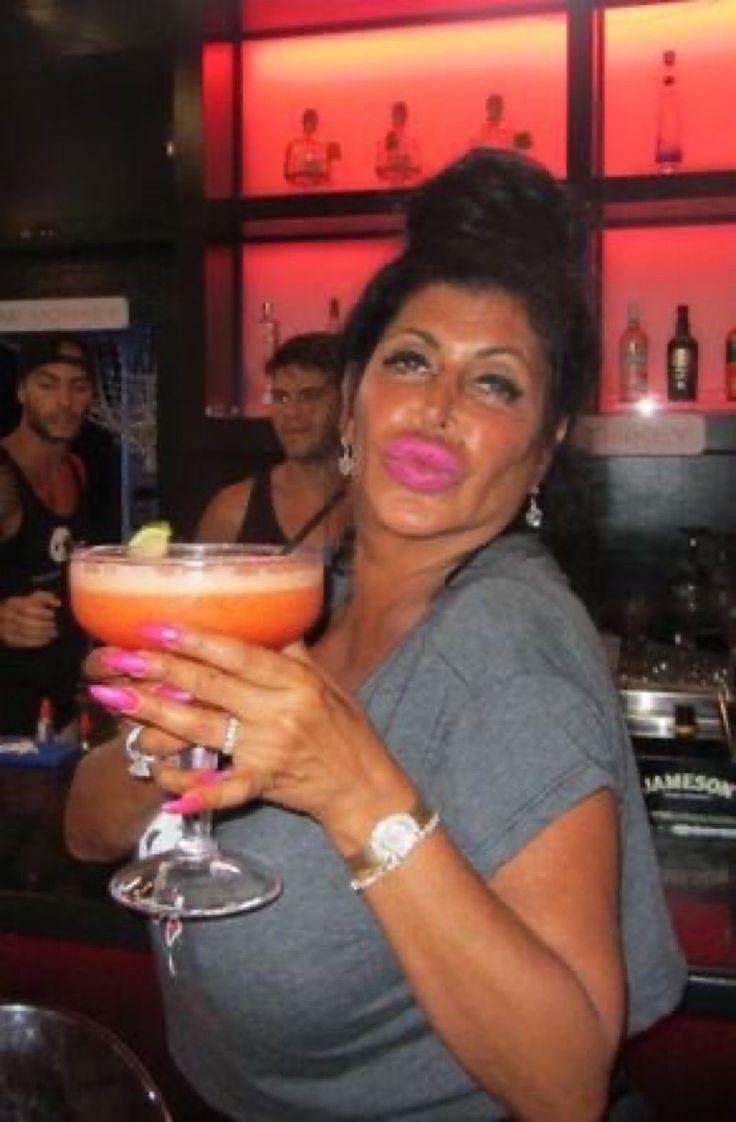 A woman at a bar raising a giant pink cocktail